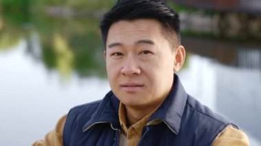 Close up of the smiled asian disabled man sitting on the wheelchair on the pier in the local lake looking at the camera. Disabled people and fishing concept
