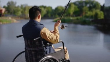 Back view of the fisherman cast a fishing rod on the pier early in the morning in the local lake alone. Disabled people and fishing concept