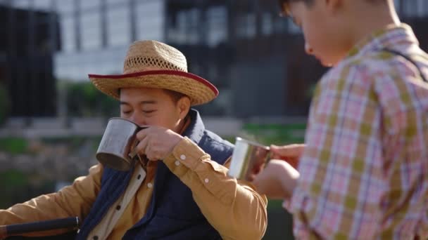 Disabled Asian Father Drinks Hot Tea His Son While Fishing — Video Stock