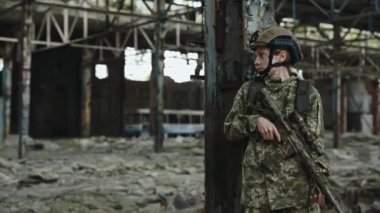 Concentrated female soldier with sniper rifle standing on abandoned factory. Brave woman wearing armour uniform and helmet. Military mission, defence and people concept.