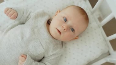 Top view of the little newborn baby lying on the cot and looking at the camera. Carefree healthy babyhood, healthcare and paediatrics care concept