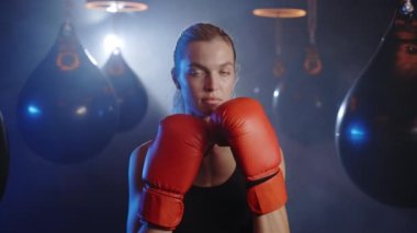 Portrait of woman kickboxer ready to punch wearing red boxing gloves standing on the sport gym background. People and boxing concept