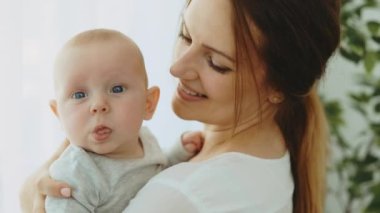 Close view of the caucasian mother carrying little baby at their new home. Portrait of the beautiful newborn baby that looking at the camera in mother hands. Motherhood concept