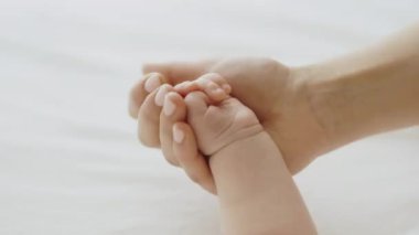 Close up above view loving mommy holds hand of her newborn baby sleeping lying on bed during healthy day nap. Cherish, mothers love and care, protection of children, adoption, babyhood concept