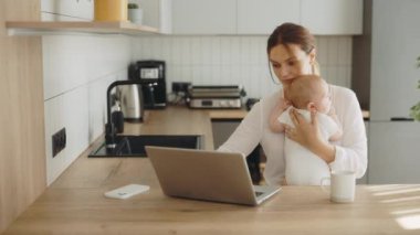 Meşgul anne evde bilgisayarın başında çalışıyor. Çalışırken kucağında bir bebek tutuyor. Teknoloji, çalışma ve stres anne kavramı