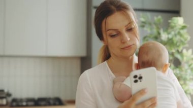Anne, bebek kucağında bir bebekle akıllı telefon üzerinde çalışıyor. Yurt içi ofiste genç bir iş. Fazla çalışan. Stres Ana kavramı