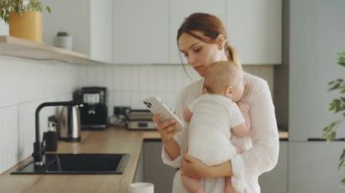 Annem telefonda çalışıyor ve kucağında tuttuğu bebeğe bakıyor. Merkez ofis. Beyaz iş kadını, çocuğunu kucağında tutarken telefonda mesajlaşıyor.