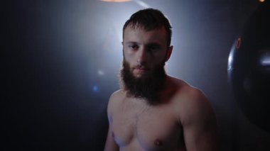 Güçlü atletik boksörün portresi, dumanlı boks salonunda kameraya bakarak antrenman yaptıktan sonra terliyor. İnsanlar ve boks kavramı