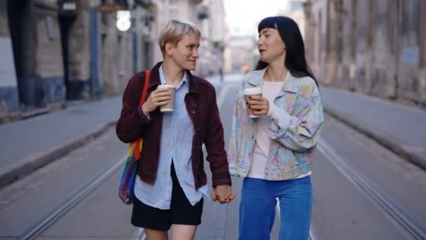 Две Лесбиянки Ходят Улице Держа Друг Друга Руки Пьют Кофе — стоковое видео