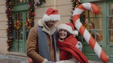 Güzel bir ailenin portresi süslenmiş caddede duruyor sıcak kıyafetler giyiyor ve Noel Baba şapkaları takıyor kameraya bakıyor. İlişkiler ve tatil konsepti.