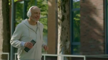 Gülümseyen mutlu erkek koşucunun yan görüntüsü koşuyor ve arka planda spor şişesini tutuyor. Spor ve sağlıklı yaşam tarzı kavramı