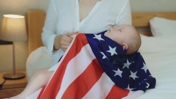 新生児はウサの旗に包まれ 母親の膝の上で寝ていると 赤ちゃんは安全に感じ 母親は男の子を撫でています 新生児と愛国心の概念 — ストック動画