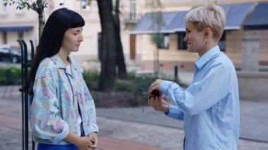 Genç lezbiyen kadın şehir merkezinde sevgili kadınına sürpriz bir evlilik teklifi yapıyor. Kadın duygusal olarak kabul ediyor ve sevgiyle sarılıyor.