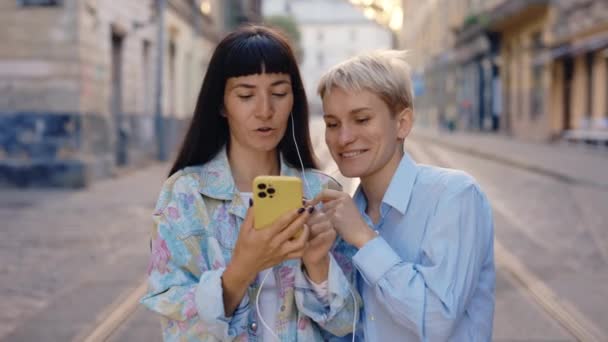 Şehir Merkezindeki Caddede Akıllı Telefon Kullanan Kulaklık Takan Aşık Lezbiyen — Stok video