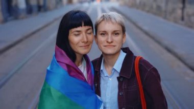 Kameraya bakan Igbt bayrağıyla lezbiyen bir çiftin portresi. Şehir merkezinde gökkuşağı bayrağıyla poz veren iki mutlu bayan arkadaş. Kadın ilişkileri, lgbt kavramı