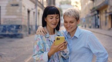 Lgbt çifti şehir merkezinde akıllı telefon kullanıyor, kulaklık takıyor. Lezbiyen aile sosyal medyayı karıştırıyor, müzik dinliyor. Lgbt insanları ve teknoloji kavramı