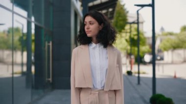 İş merkezinin yakınında kameraya bakarak ellerini çaprazlayan resmi kıyafetli güzel, kıvırcık, genç iş kadınının portresi. Halk ve iş kavramı