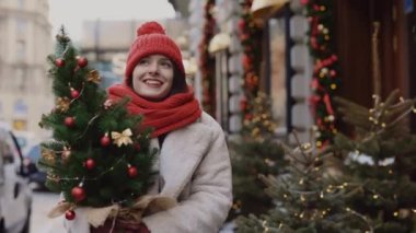 Süslü caddede kırmızı şapka ve eşarp takarak yürüyen mutlu bir kız. İnsanlar ve Noel tatili konsepti