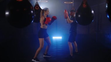 Beyaz kadın, boks salonunun dumanlı boks salonunda kişisel antrenörüyle gölge boksu yaparak antrenman yapıyor. İnsanlar ve spor konsepti