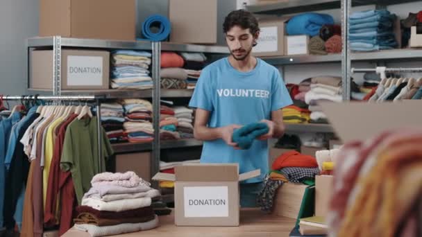 Кавказский Волонтер Внимательно Держит Коробку Одеждой Пожертвований Сортировки Одежды Полки — стоковое видео