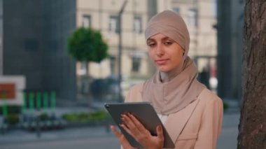Arap iş kadınının başörtüsü takan portresi ve iş merkezinin yanında çalışma amacıyla tablet kullanarak oturan resmi kıyafet.