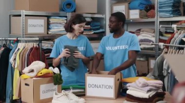 Esmer kadın depoda duruyor ve bağış için kıyafet düzenlerken erkek arkadaşıyla konuşuyor. Arka plandaki raflara aitti. İnsani yardım kavramı