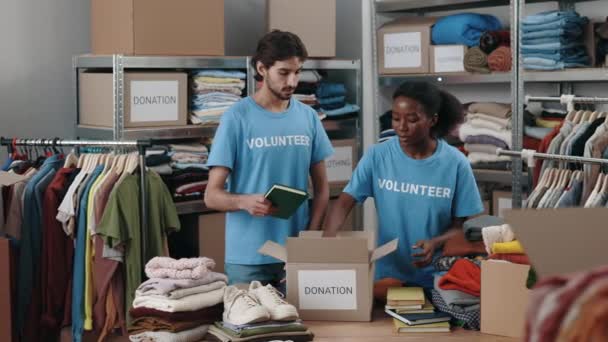 忙しい白人男性と女性の寄付センターの労働者は倉庫や梱包箱に注文したスタッフと一緒に立って働いています ボランティア業界と人道支援の概念 — ストック動画