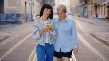 Lgbt çifti şehir merkezinde akıllı telefon ve kaydırma uygulamaları kullanarak yürüyor. Lezbiyen aile sosyal medyayı karıştırıyor, tartışıyor, bir şeyler gösteriyor. Lgbt insanları ve teknoloji kavramı