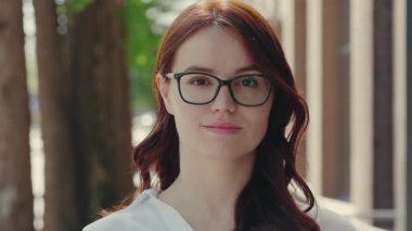İş merkezinin yakınında kameraya gözlüklü, resmi takım elbiseli, gülümseyen kızıl saçlı güzel kadının portresi. Halk ve iş kavramı