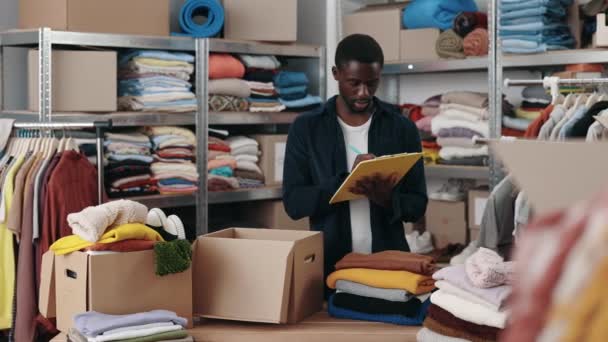 Afrikanische Männliche Freiwillige Machen Sich Notizen Während Sie Kleidung Sortieren — Stockvideo