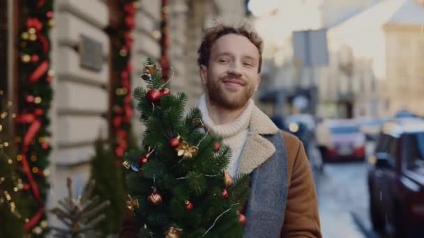 Lächelnder Kaukasier Kommt Vom Christbaumladen Mit Dem Kleinen Weihnachtsbaum Nach — Stockvideo