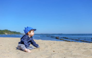 Polonya 'da plajda oturan beyzbol şapkalı küçük çocuk.