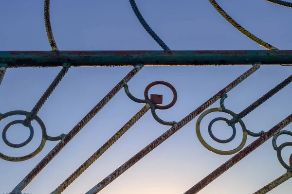 A fragment of a metal gate against the sky and the rising sun in Poland