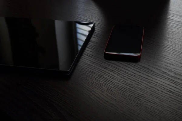 Tablet and mobile phone lying on the wooden table in the dark