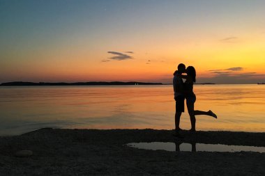 Sahilde, güzel gün batımında mutlu insanların siluetleri..