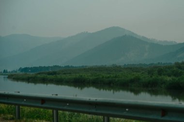 Dağlar ve ormanlar yakınlarda bir nehir ve önünde bir yol bariyeri, dağlarda sis.