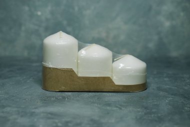 Karton bir kutuda üç farklı boyutta üç beyaz mum seti ve gri bir arka planda şeffaf bir film..