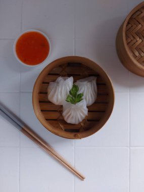 Seçici odak Hakau ya da şeffaf kabuklu Dim Sum dolu karides. Geleneksel Çin yemekleri. Bambu ahşap buharlı vapurda servis edilmiş. Biber sosu ve çubukla tamamlanmış. Kerevizle süslenmiş..