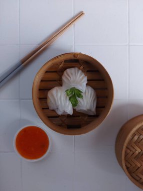 Seçici odak Hakau ya da şeffaf kabuklu Dim Sum dolu karides. Geleneksel Çin yemekleri. Bambu ahşap buharlı vapurda servis edilmiş. Biber sosu ve çubukla tamamlanmış. Kerevizle süslenmiş..