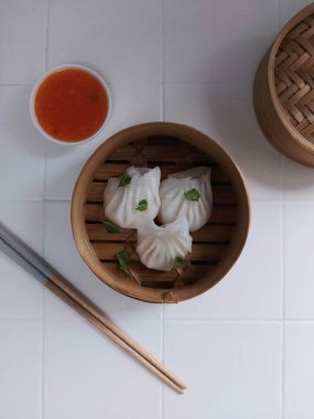 Seçici odak Hakau ya da şeffaf kabuklu Dim Sum dolu karides. Geleneksel Çin yemekleri. Bambu ahşap buharlı vapurda servis edilmiş. Biber sosu ve çubukla tamamlanmış. Kerevizle süslenmiş..