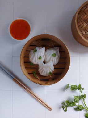 Seçici odak Hakau ya da şeffaf kabuklu Dim Sum dolu karides. Geleneksel Çin yemekleri. Bambu ahşap buharlı vapurda servis edilmiş. Biber sosu ve çubukla tamamlanmış. Kerevizle süslenmiş..