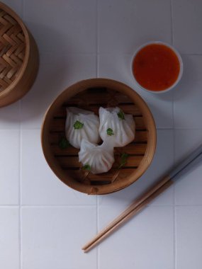 Seçici odak Hakau ya da şeffaf kabuklu Dim Sum dolu karides. Geleneksel Çin yemekleri. Bambu ahşap buharlı vapurda servis edilmiş. Biber sosu ve çubukla tamamlanmış. Kerevizle süslenmiş..