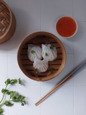 Seçici odak Hakau ya da şeffaf kabuklu Dim Sum dolu karides. Geleneksel Çin yemekleri. Bambu ahşap buharlı vapurda servis edilmiş. Biber sosu ve çubukla tamamlanmış. Kerevizle süslenmiş..