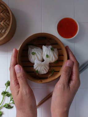 Seçici odak Hakau ya da şeffaf kabuklu Dim Sum dolu karides. Geleneksel Çin yemekleri. Bambu ahşap buharlı vapurda servis edilmiş. Biber sosu ve çubukla tamamlanmış. Kerevizle süslenmiş..