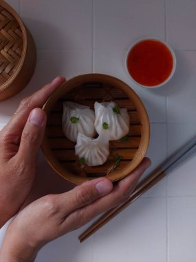Seçici odak Hakau ya da şeffaf kabuklu Dim Sum dolu karides. Geleneksel Çin yemekleri. Bambu ahşap buharlı vapurda servis edilmiş. Biber sosu ve çubukla tamamlanmış. Kerevizle süslenmiş..