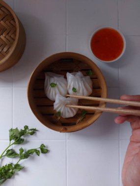 Seçici odak Hakau ya da şeffaf kabuklu Dim Sum dolu karides. Geleneksel Çin yemekleri. Bambu ahşap buharlı vapurda servis edilmiş. Biber sosu ve çubukla tamamlanmış. Kerevizle süslenmiş..