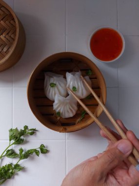 Seçici odak Hakau ya da şeffaf kabuklu Dim Sum dolu karides. Geleneksel Çin yemekleri. Bambu ahşap buharlı vapurda servis edilmiş. Biber sosu ve çubukla tamamlanmış. Kerevizle süslenmiş..