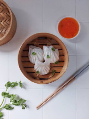 Seçici odak Hakau ya da şeffaf kabuklu Dim Sum dolu karides. Geleneksel Çin yemekleri. Bambu ahşap buharlı vapurda servis edilmiş. Biber sosu ve çubukla tamamlanmış. Kerevizle süslenmiş..