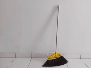 Bogor, Endonezya-11 Mart 2022: Beyaz fayanslı zeminde beyaz bir duvara yaslanmış bir süpürge. Metin ya da alıntı için çok yer