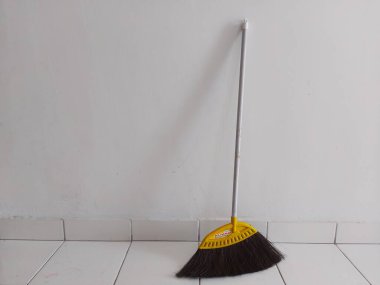 Bogor, Endonezya-11 Mart 2022: Beyaz fayanslı zeminde beyaz bir duvara yaslanmış bir süpürge. Metin ya da alıntı için çok yer